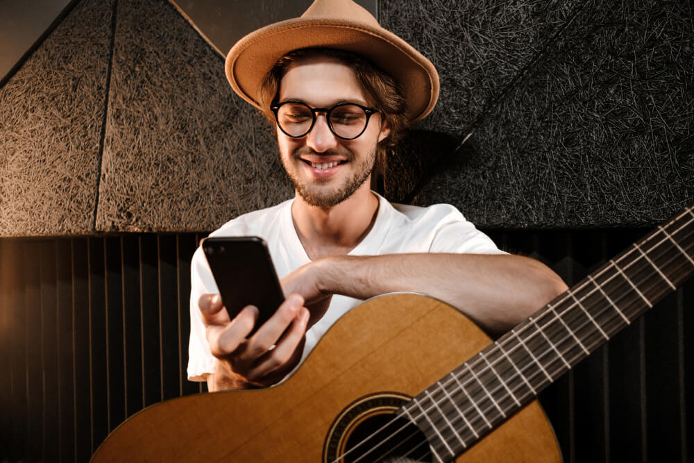 young male guitarist playing the guitar while looking at the guitar2tabs app